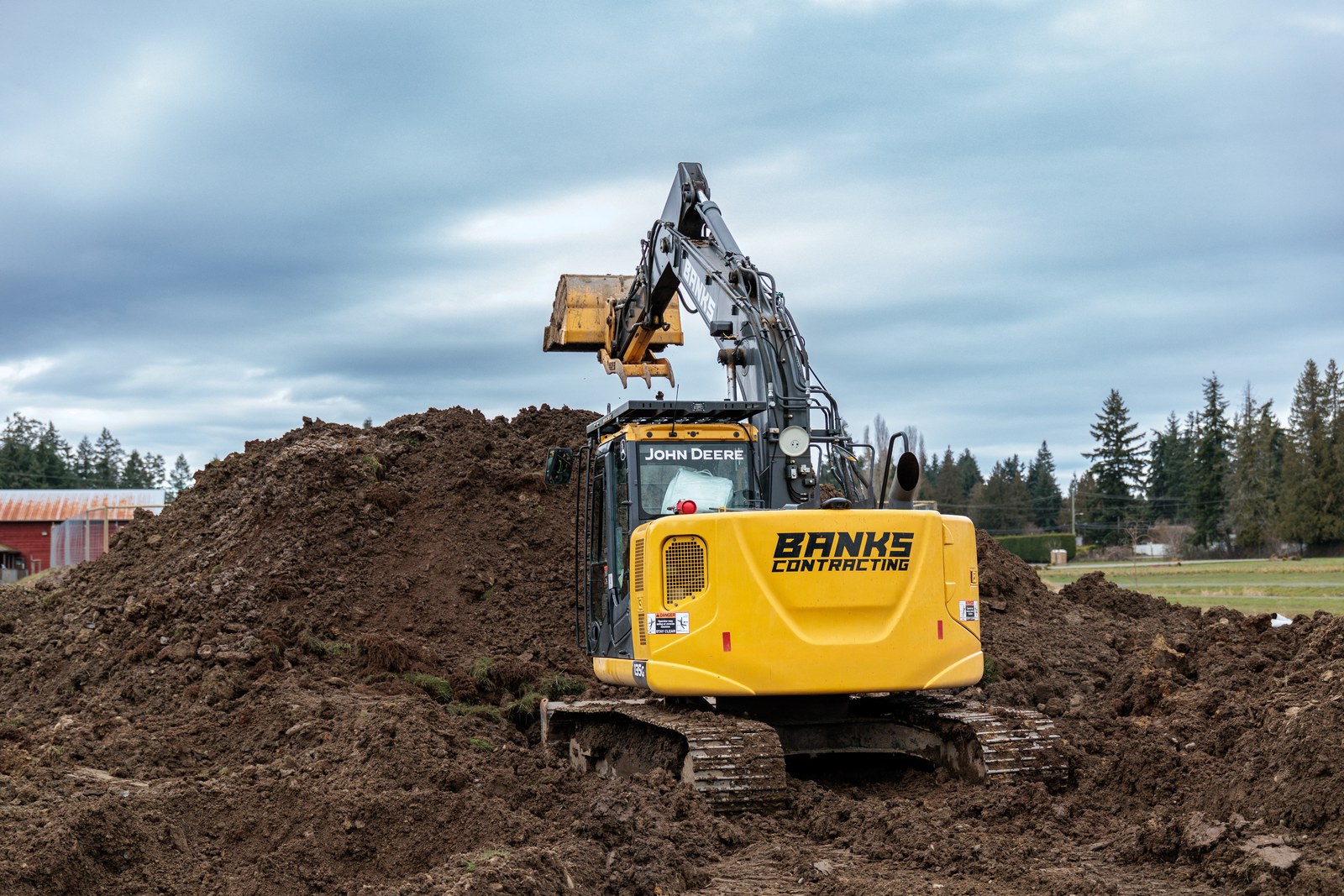 The yellow rear of a Banks Contracting excavator faces a pile of earth with its bucket raised above