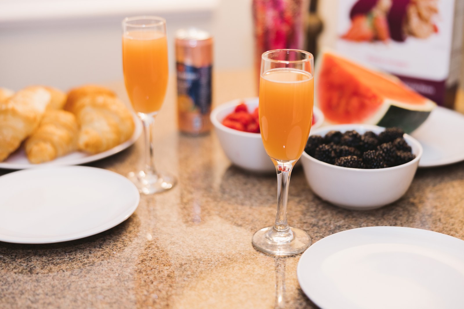 Glasses of orange juice sit beside croissants and bowls of berries on a breakfast counter