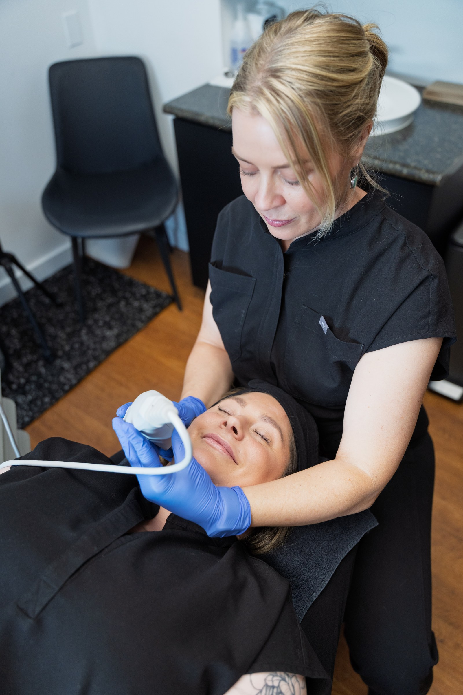 Practitioner using a handheld skincare device on a reclining client’s cheek