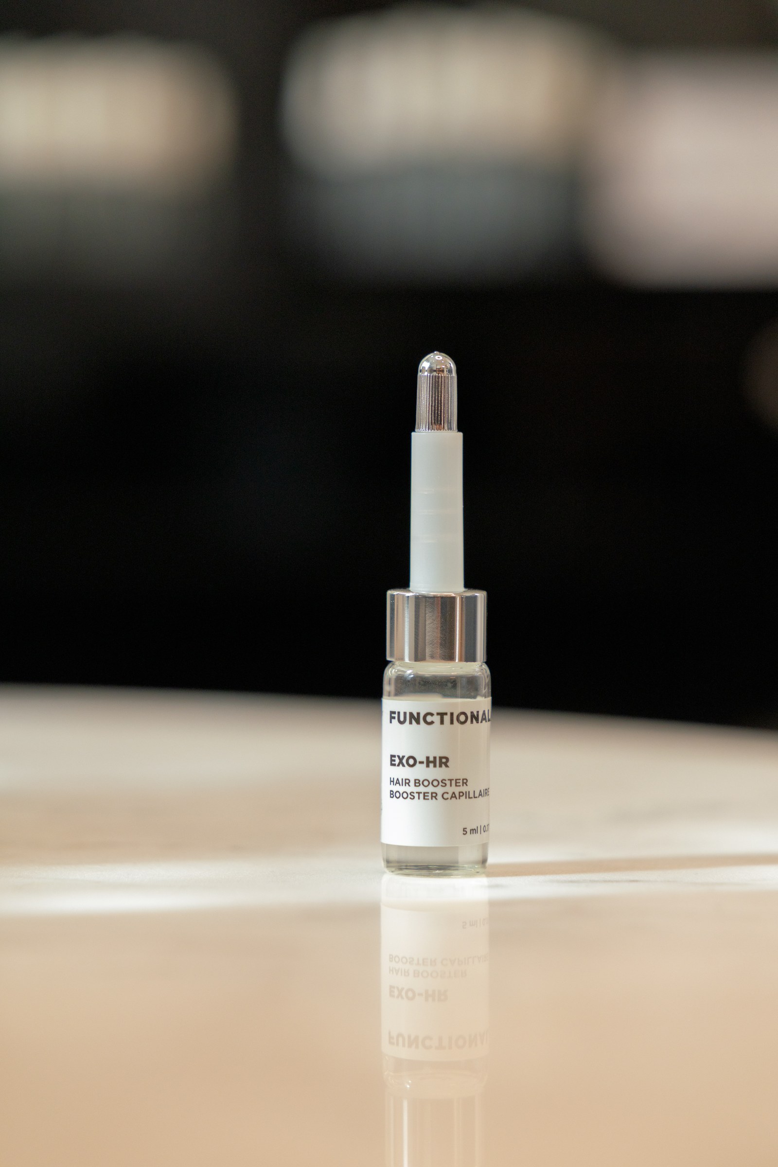 A glass bottle of Functionalab EXO-HR hair booster stands on a reflective pale counter