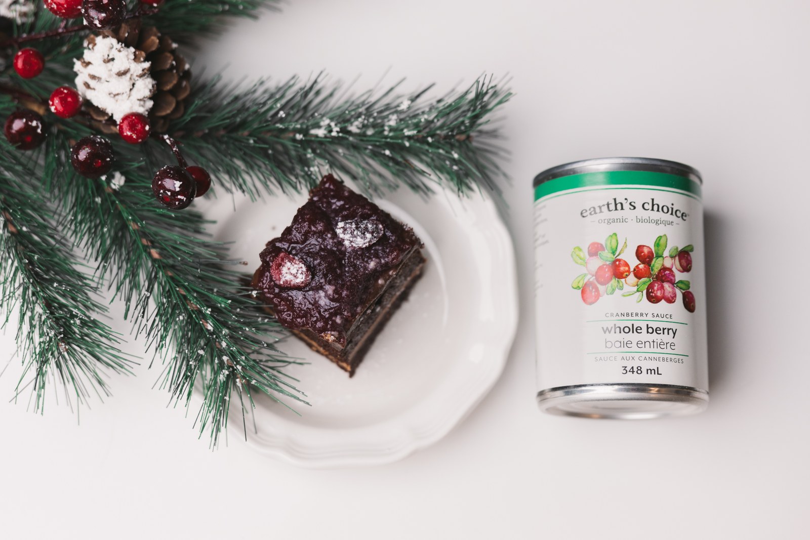 Earth’s Choice cranberry sauce beside a plated dessert and evergreen branches on a white surface