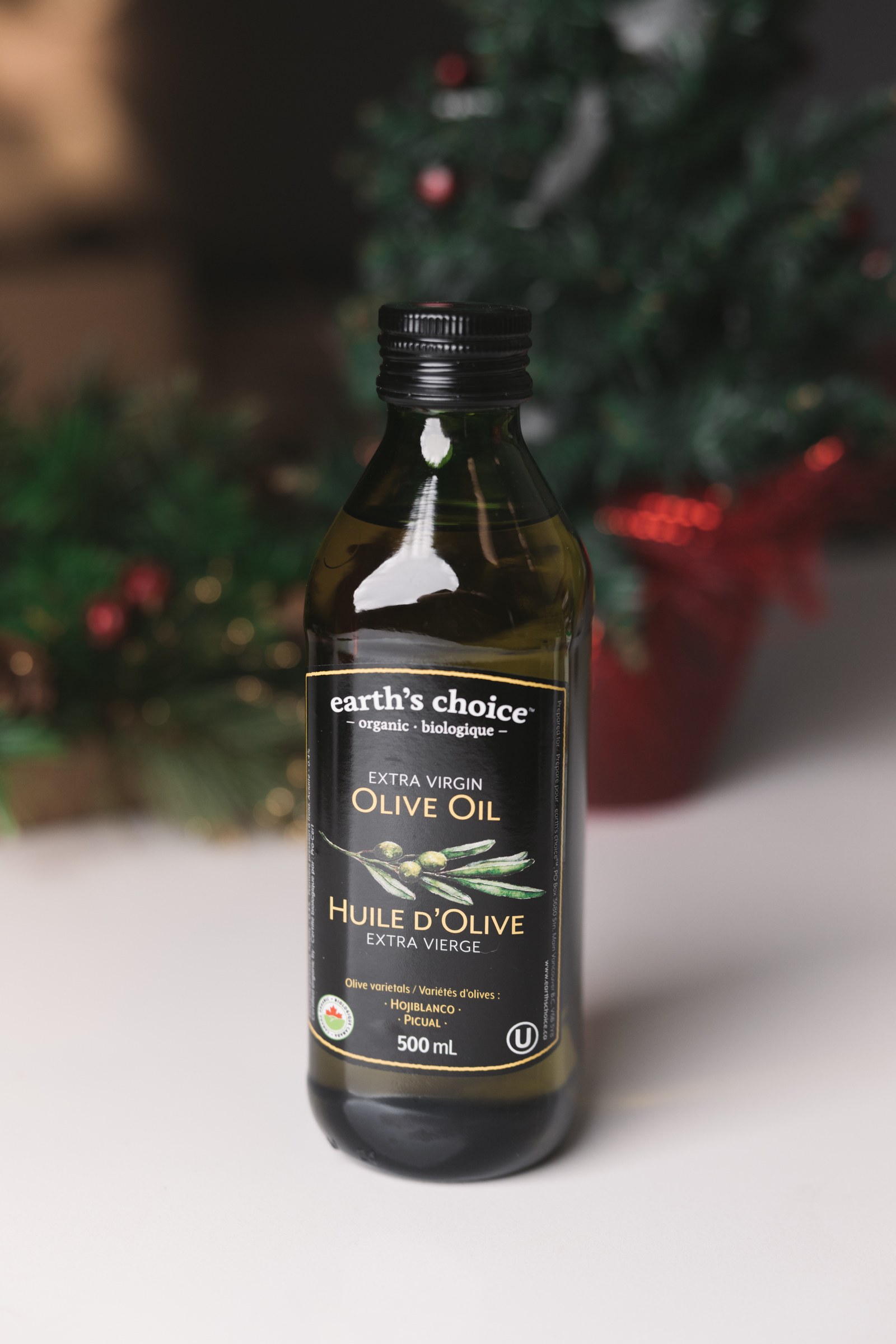 Bottle of Earth’s Choice extra virgin olive oil against a softly lit holiday arrangement