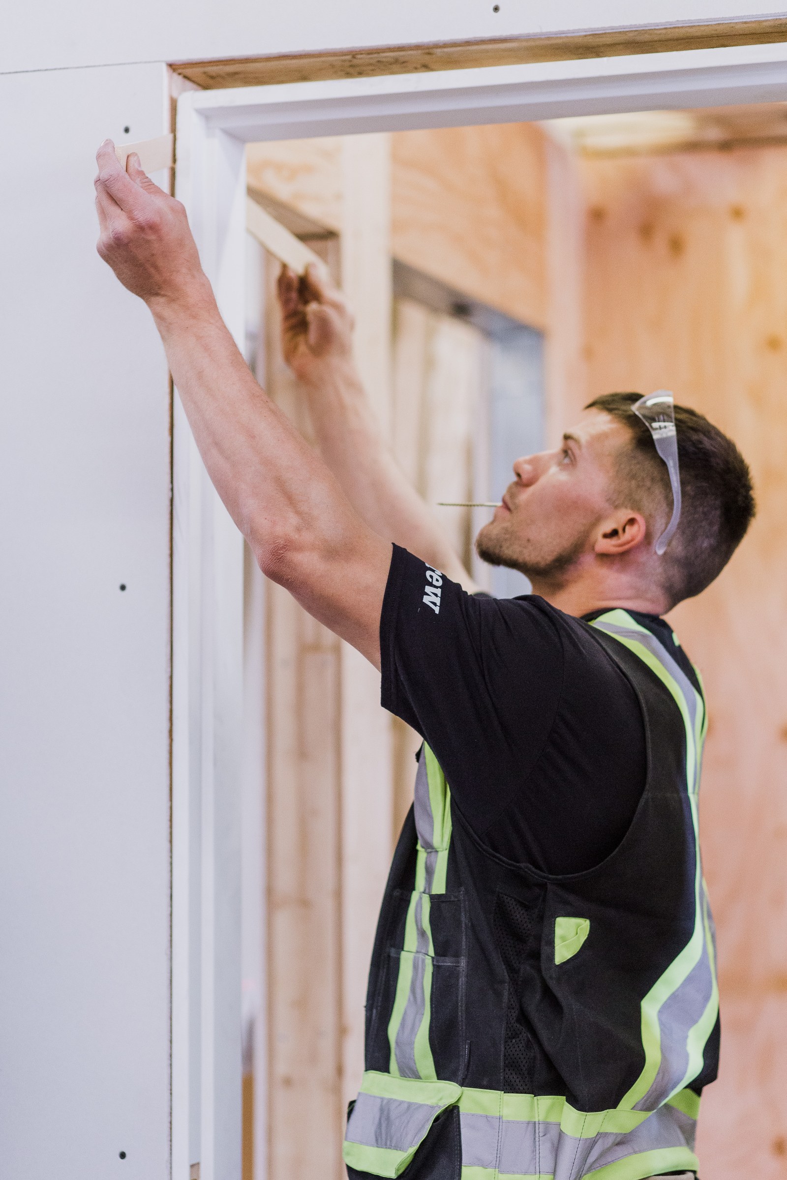 A carpenter fits a white strip of trim across the top of a doorway