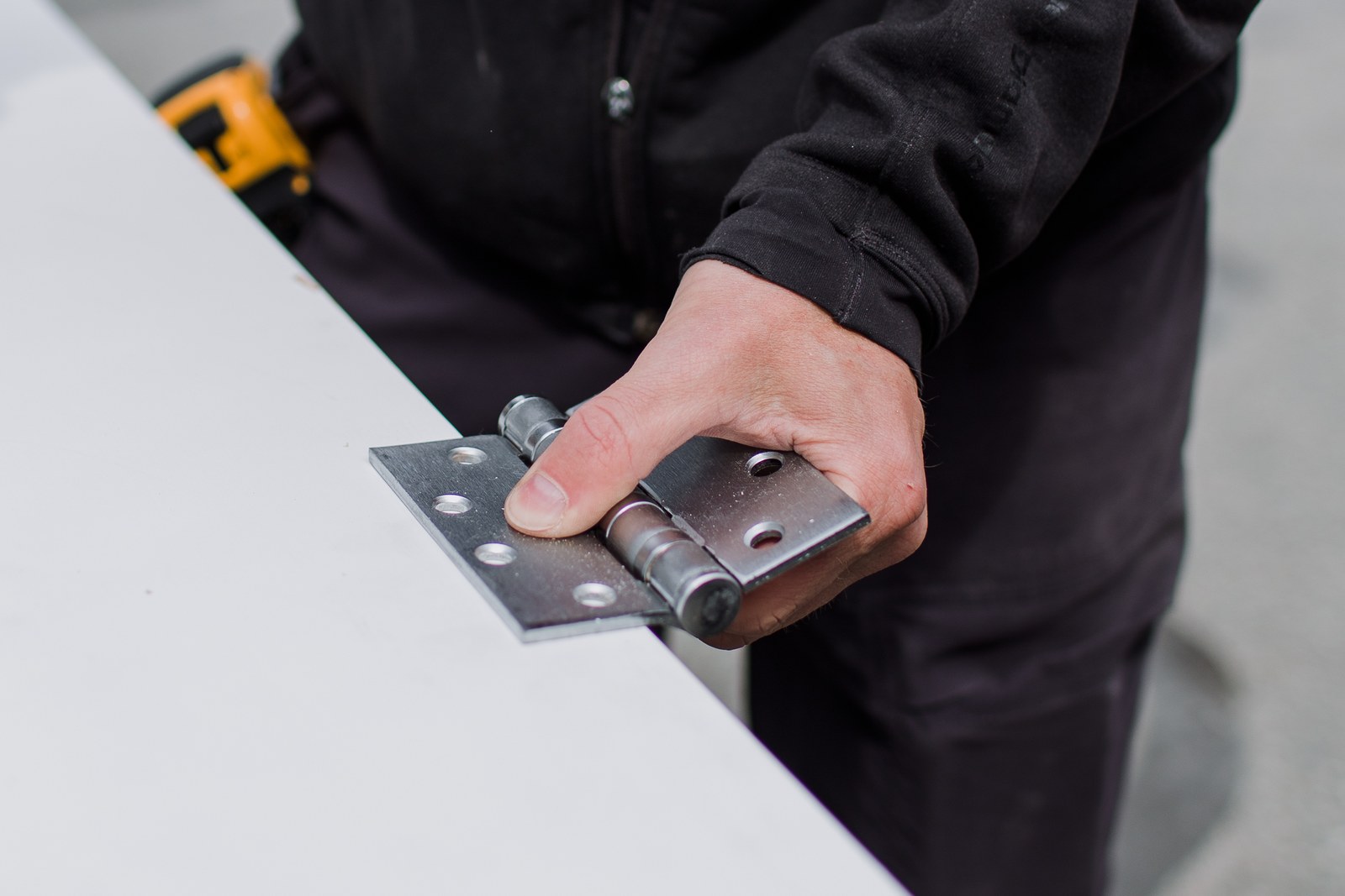 A carpenter holds a metal door hinge against the edge of a white door
