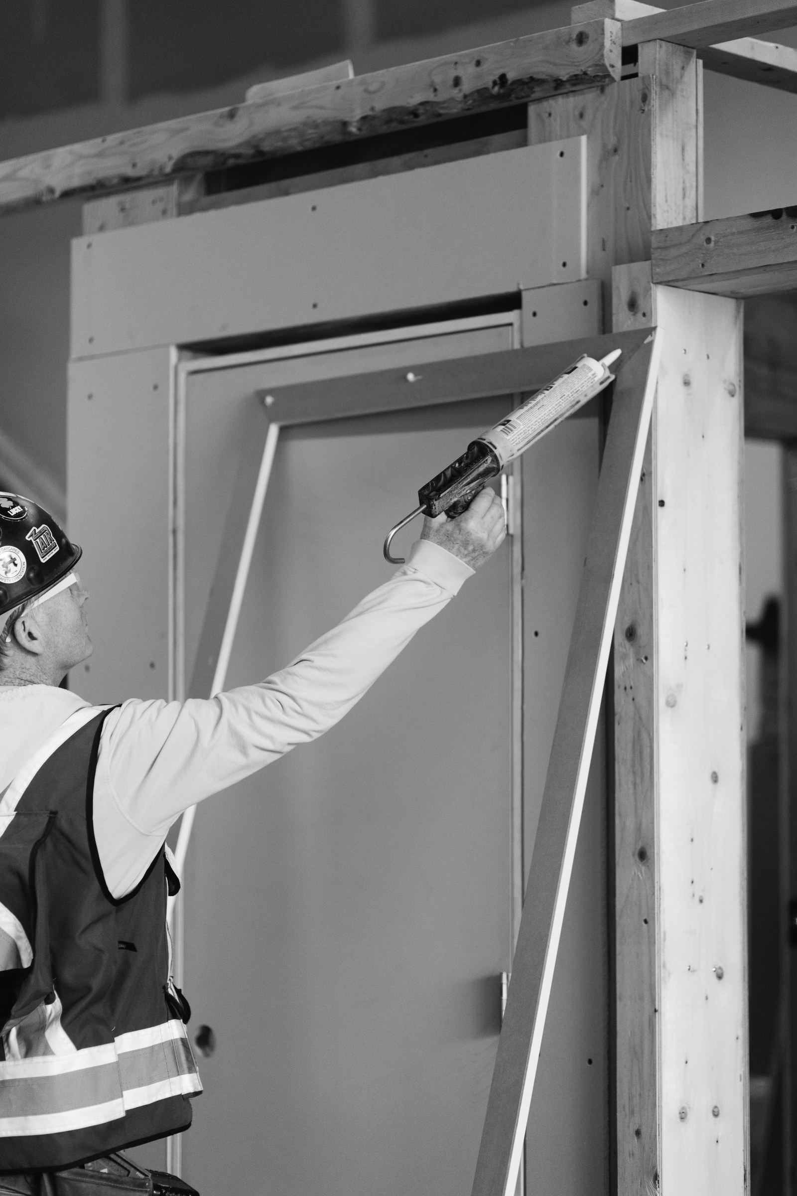 Black and white photograph of a carpenter applying adhesive to a long piece of white door trim