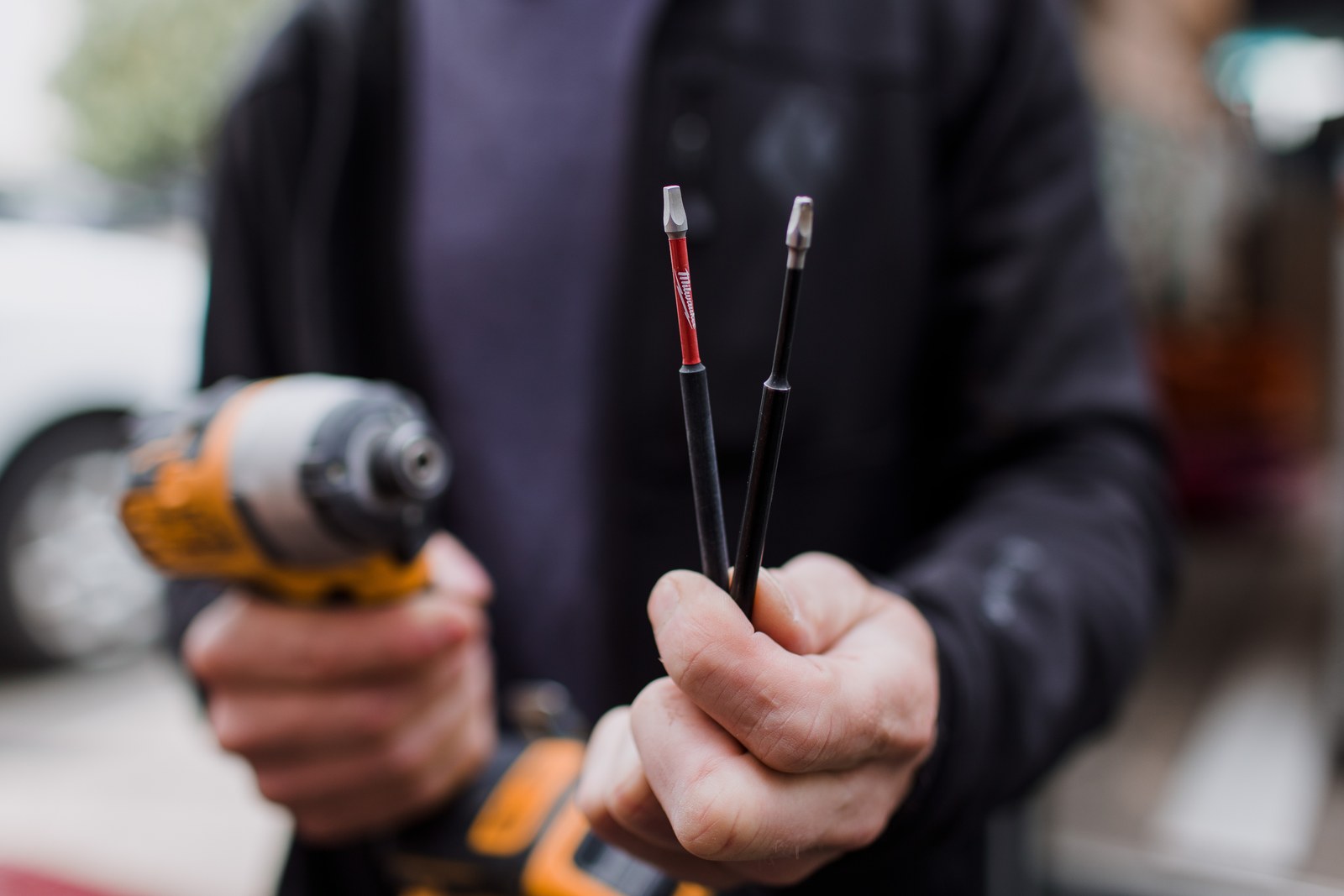 A carpenter holds a yellow cordless drill and two long driver bits