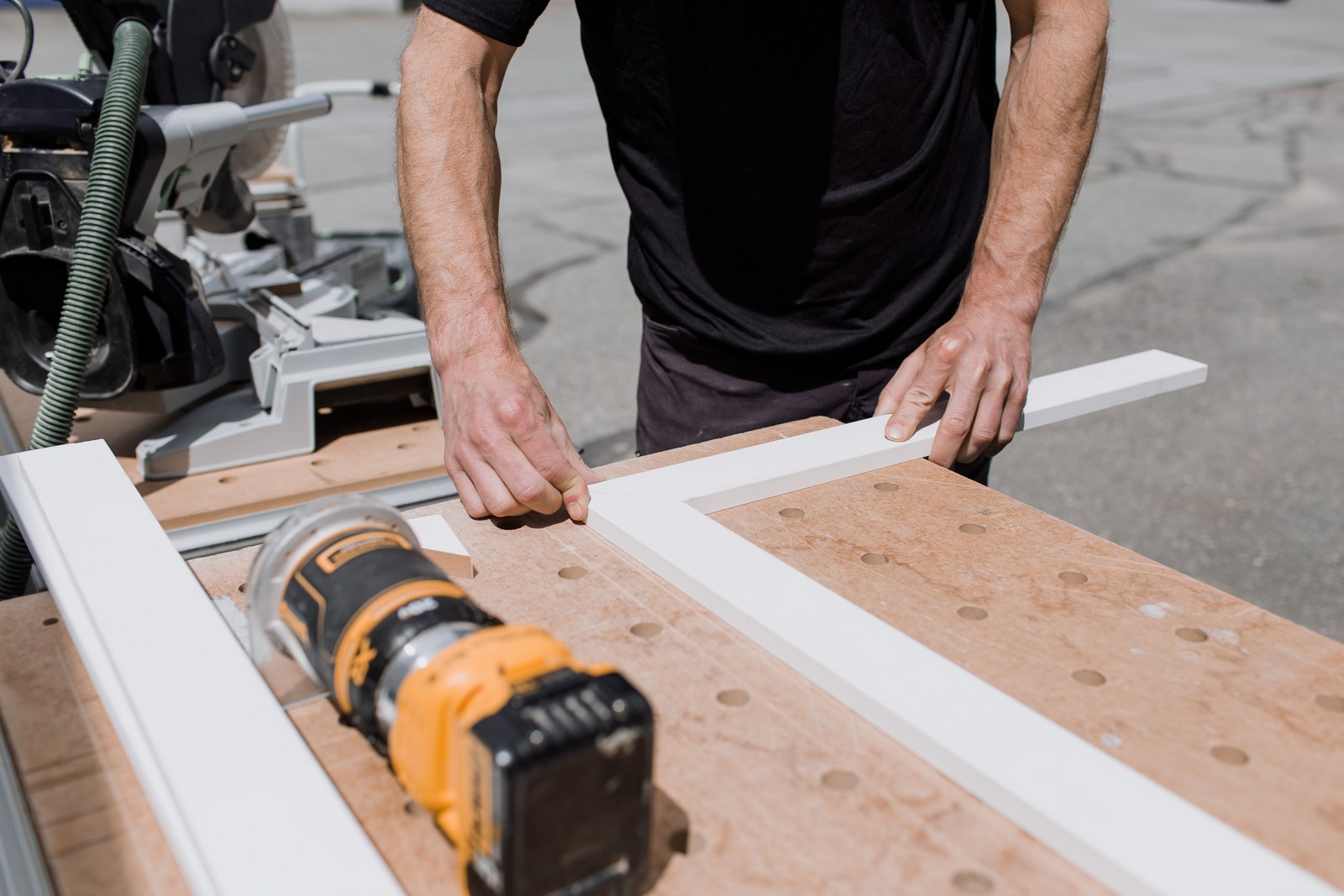 A carpenter aligns white trim on a workbench beside a cordless drill
