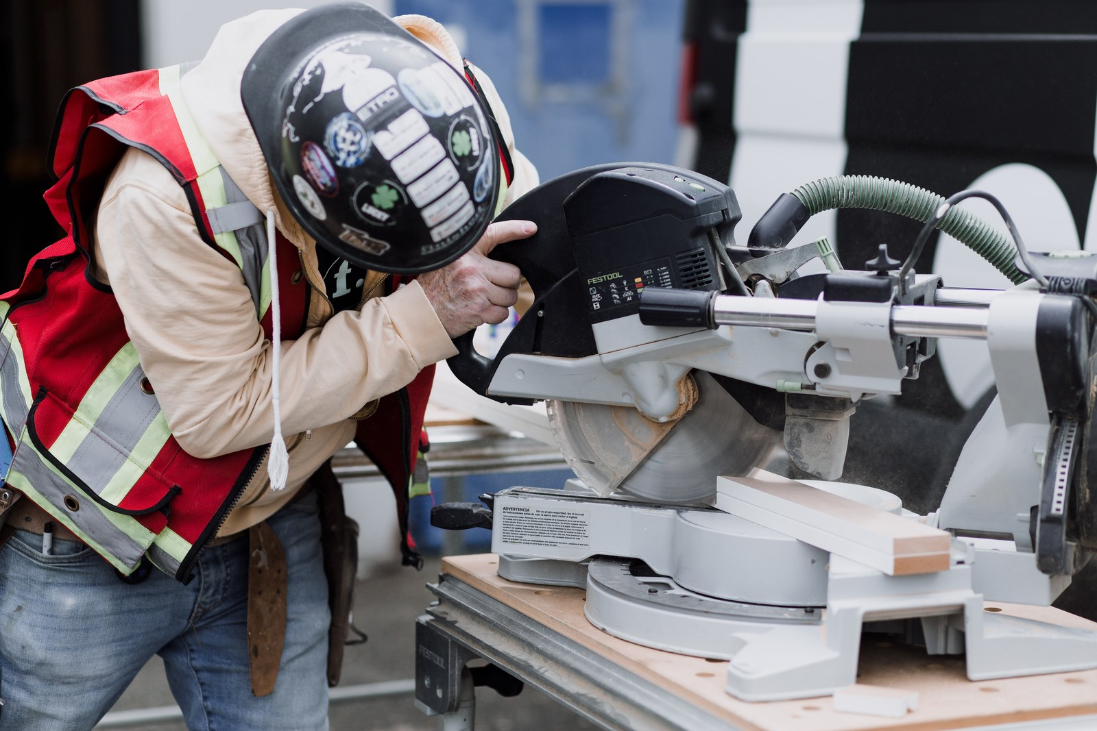 A carpenter in a hard hat and high-visibility vest cuts white trim with a sliding mitre saw