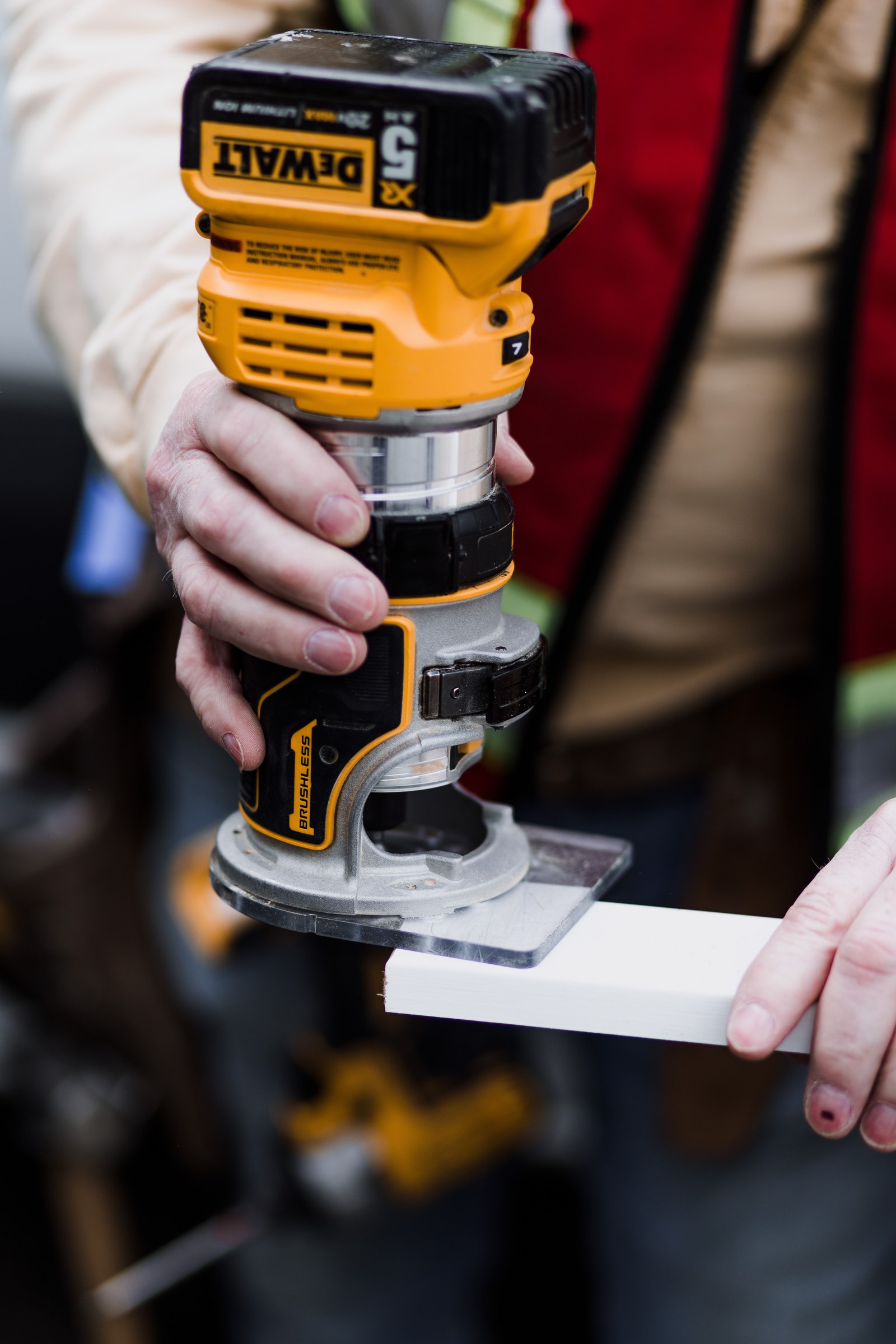 A carpenter guides a yellow cordless router along the edge of white trim
