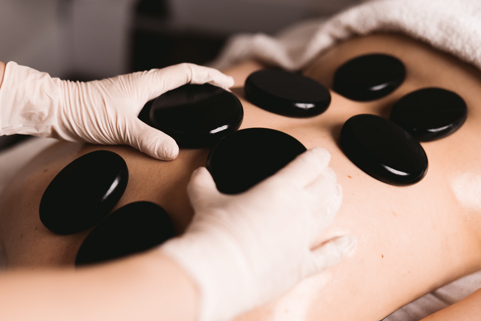 A practitioner places smooth black stones on a client's back during a spa treatment