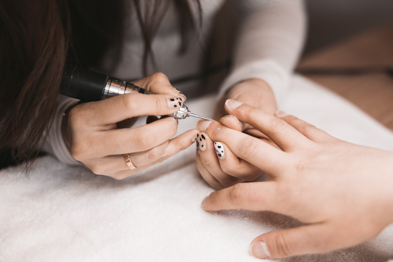 A nail technician uses a small electric manicure tool on a client's fingernail