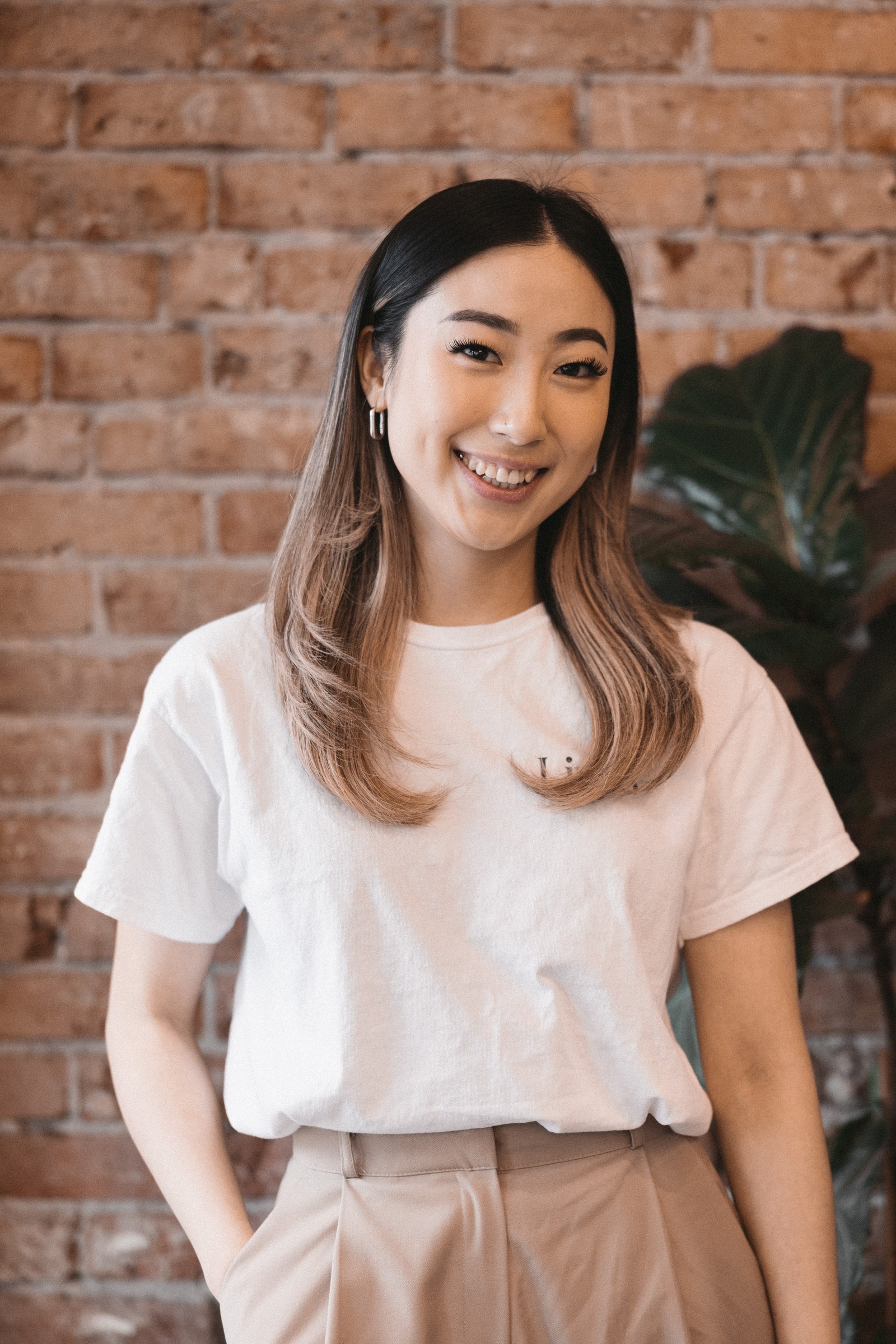 A smiling Liveo team member in a white shirt stands beside exposed brick and a plant