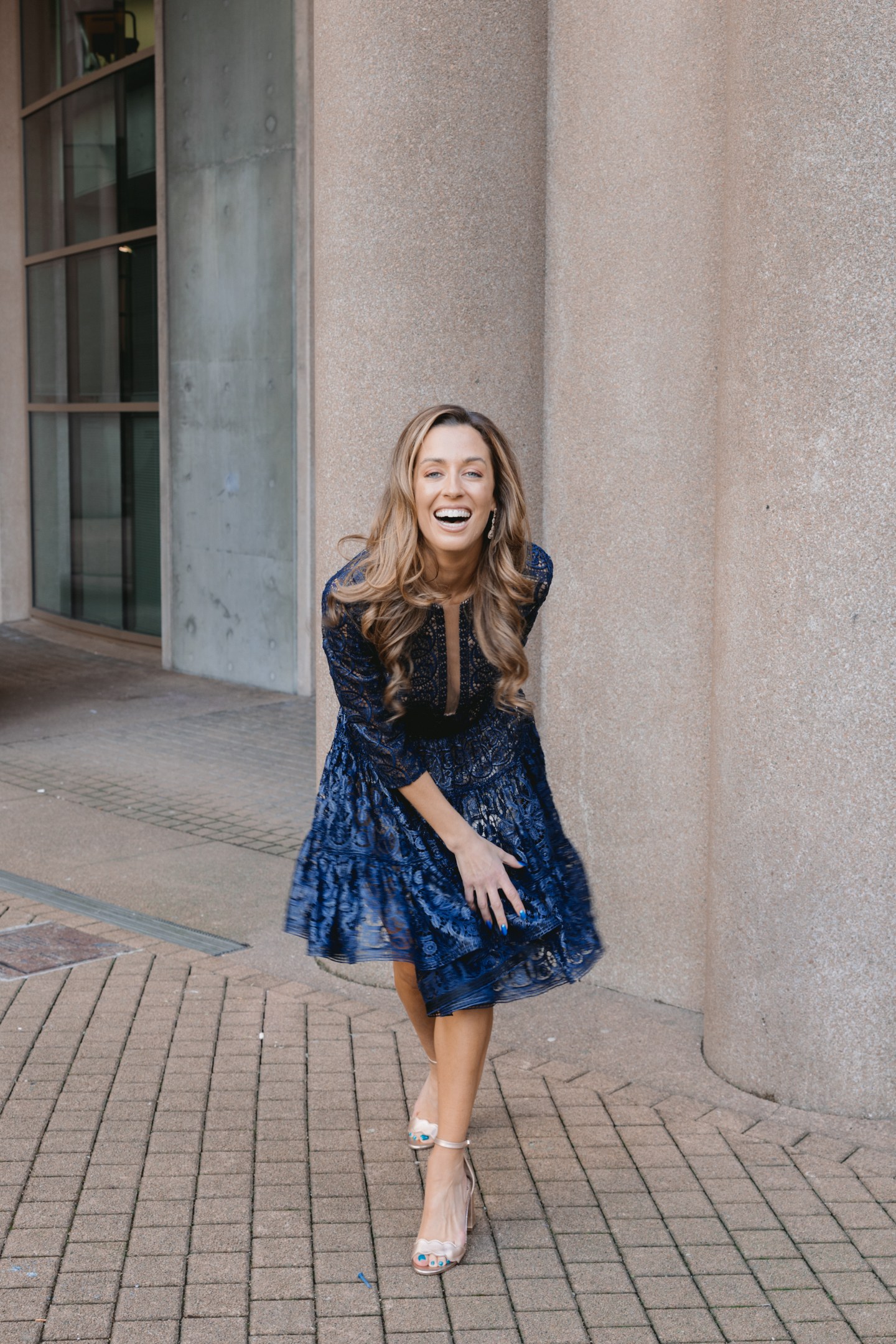 Laughing woman wearing a blue patterned dress beside stone columns