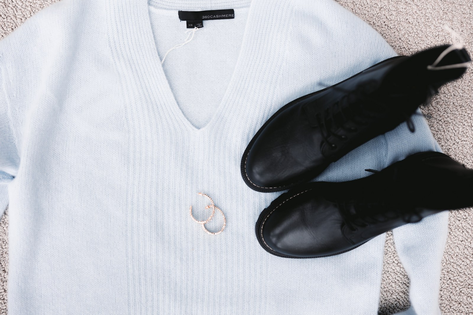 Black lace-up boots and hoop earrings arranged on a white knit sweater