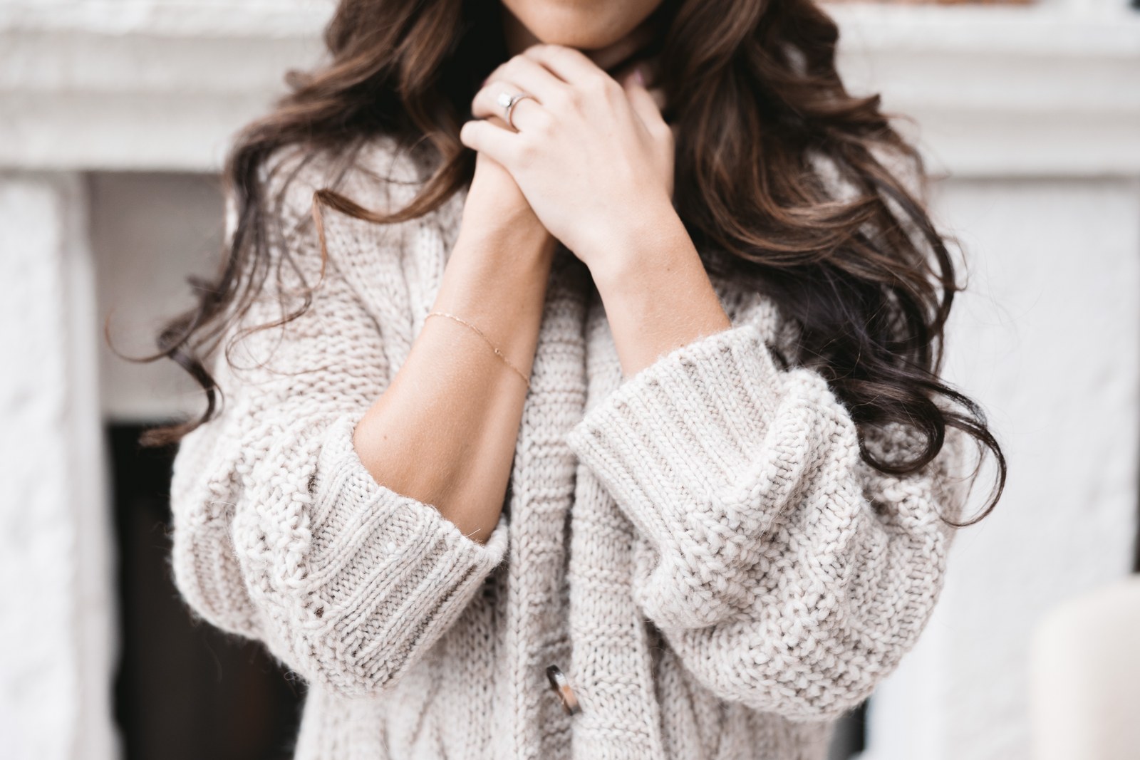 Close-up of a cream knit cardigan with the model’s hands near the collar