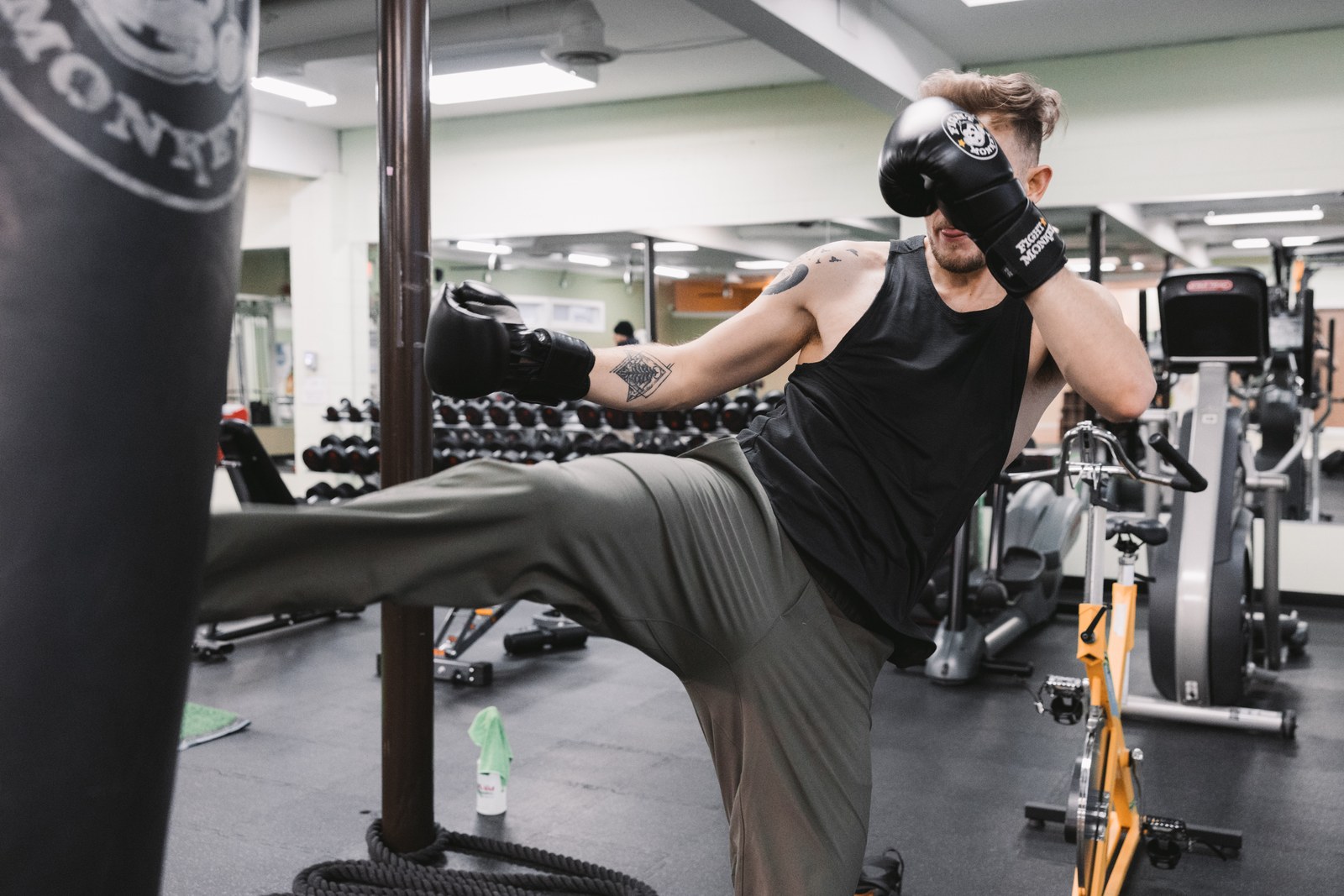 Man wearing boxing gloves kicking a black punching bag inside a gym