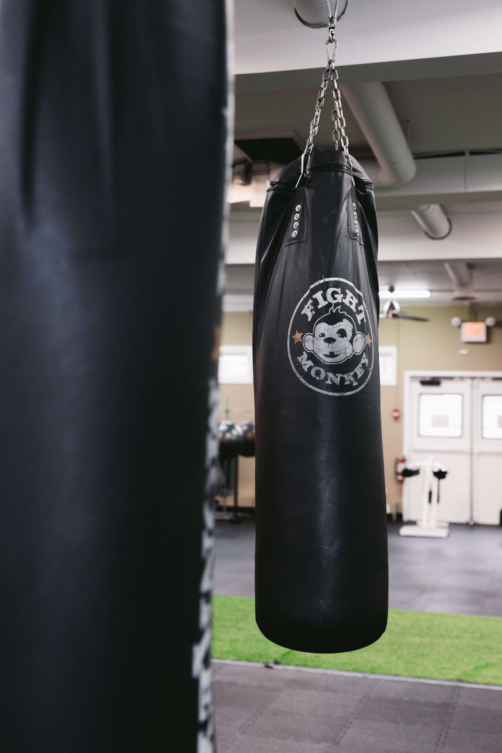 Black punching bag hanging beside green gym turf