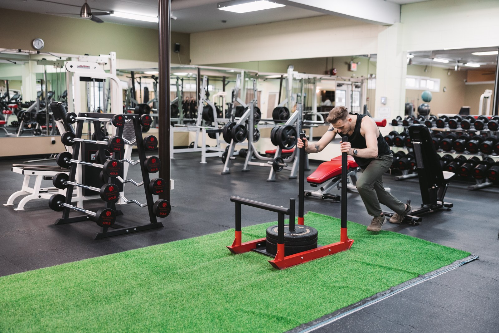 Man pushing a weighted training sled across green turf inside a gym