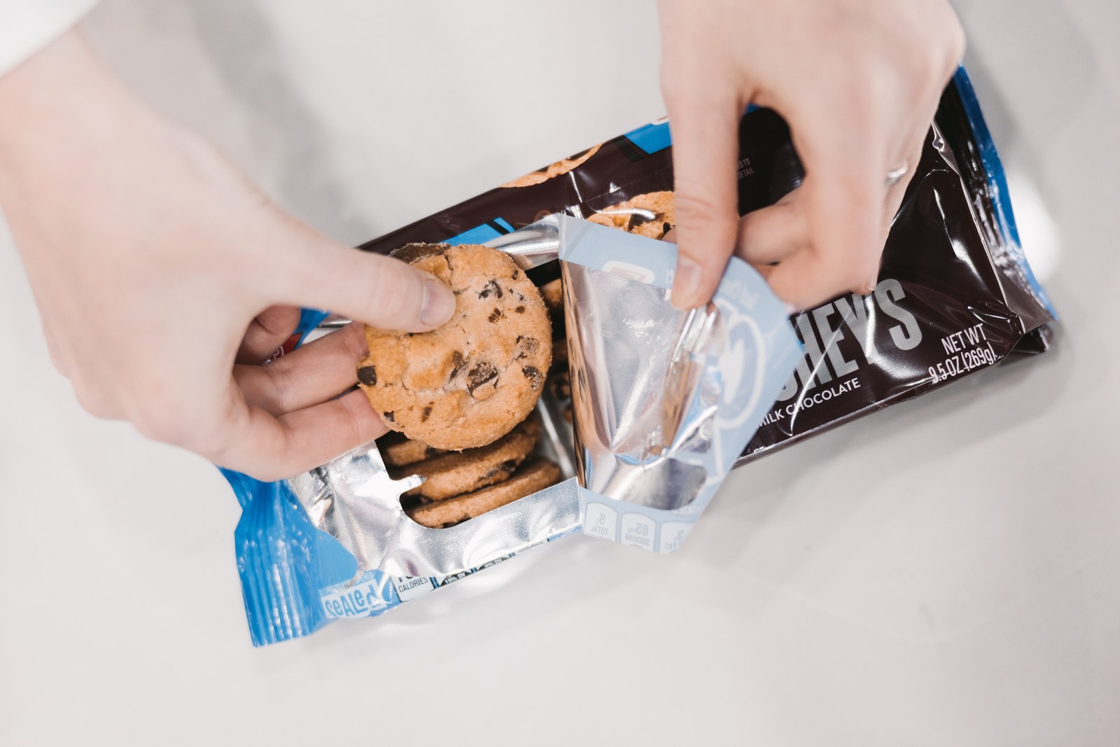 Hands taking a chocolate chip cookie from an opened blue and brown package