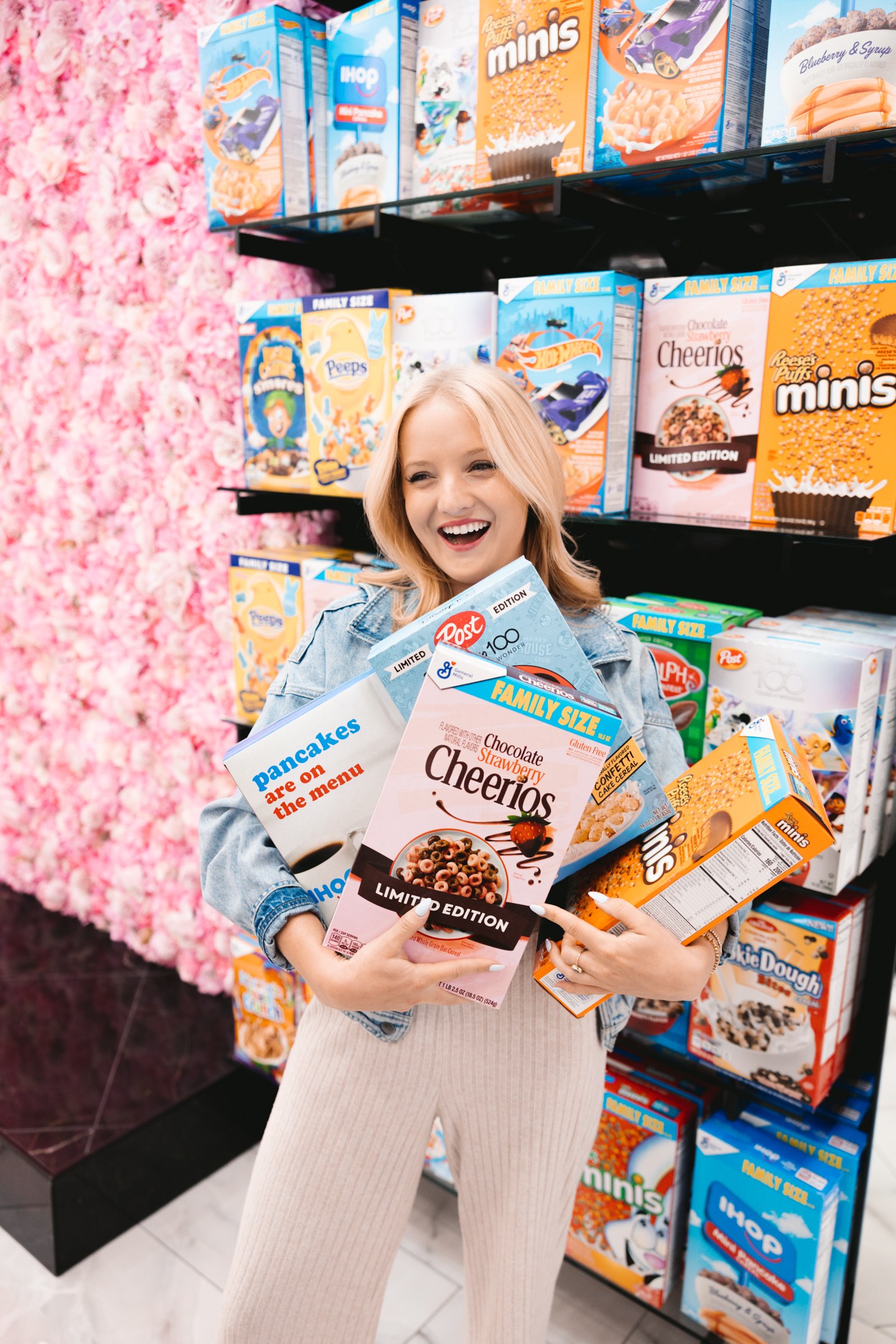 Smiling woman holding cereal boxes beside colourful shop shelves