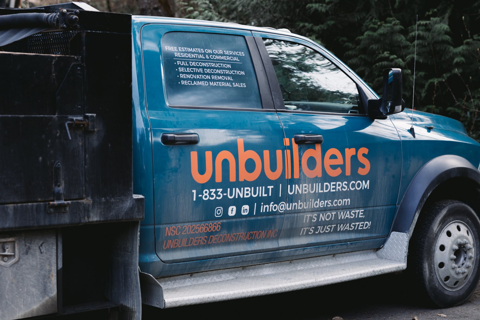 A blue Unbuilders work truck with orange lettering is parked beside trees at a job site