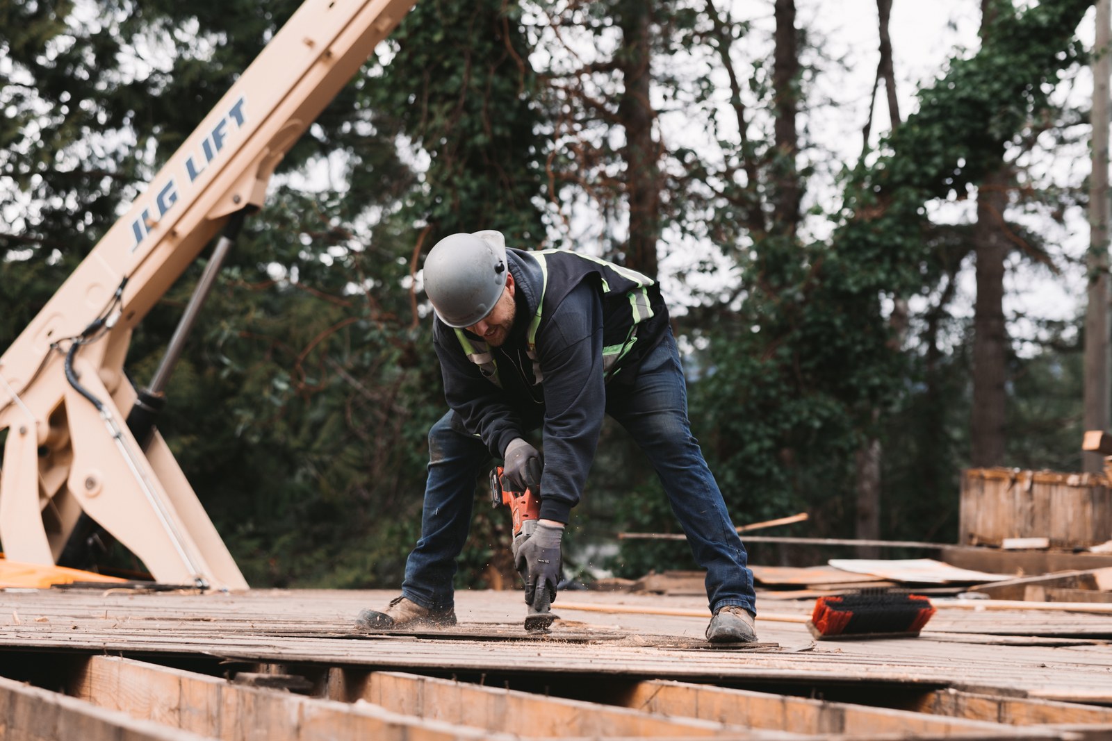 An Unbuilders crew member uses a reciprocating saw on timber floorboards beside a boom lift