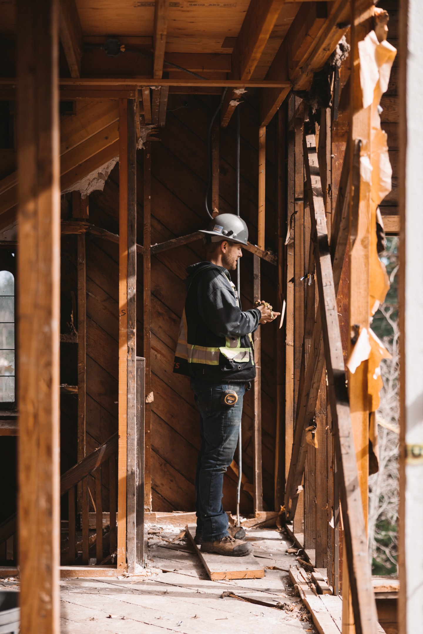 A crew member in a hard hat works inside the exposed timber walls of a building